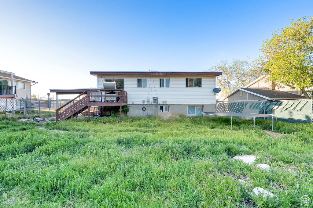 Back of house featuring stairs, a trampoline, fence, and a wooden deck
