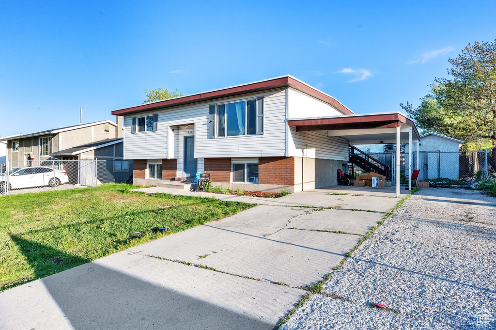 Raised ranch with a front lawn, fence, an attached carport, and concrete driveway