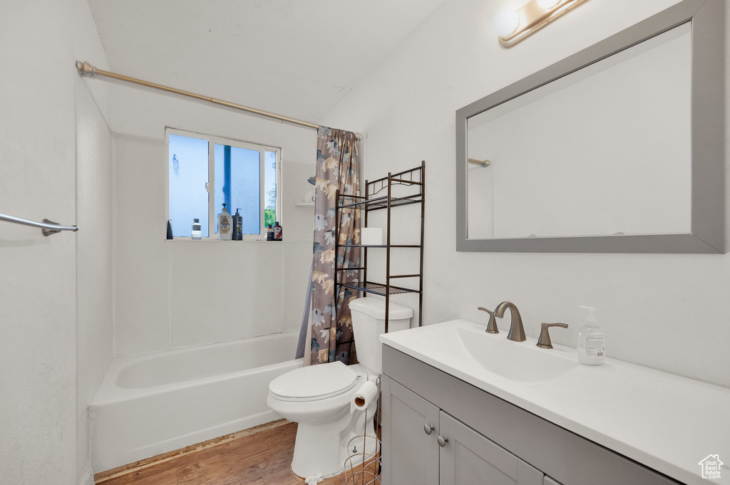 Bathroom with vanity, shower / bathtub combination with curtain, wood finished floors, and toilet