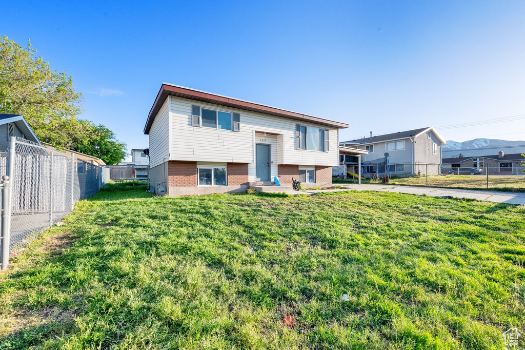 Raised ranch with brick siding, a front yard, a fenced backyard, entry steps, and concrete driveway