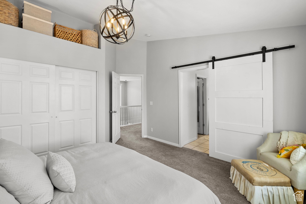 Carpeted bedroom featuring a closet, a barn door, baseboards, and a chandelier