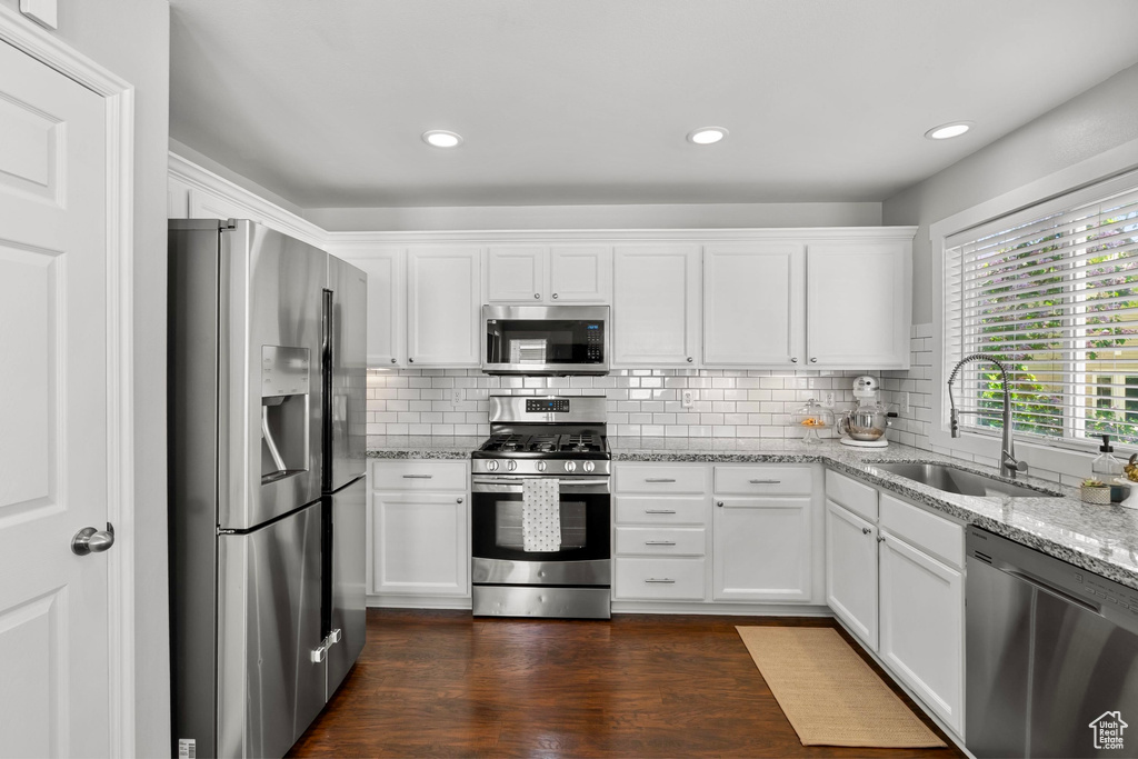 Kitchen with a sink, decorative backsplash, appliances with stainless steel finishes, and white cabinets