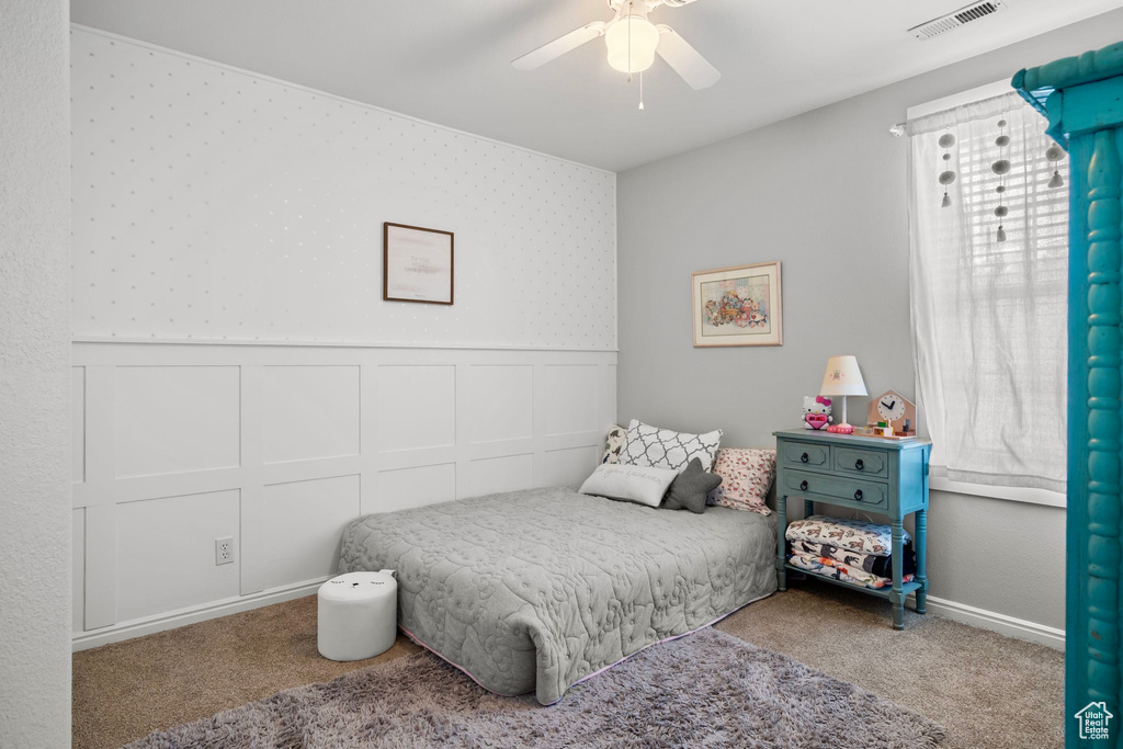 Bedroom featuring a ceiling fan, visible vents, carpet, and a wainscoted wall