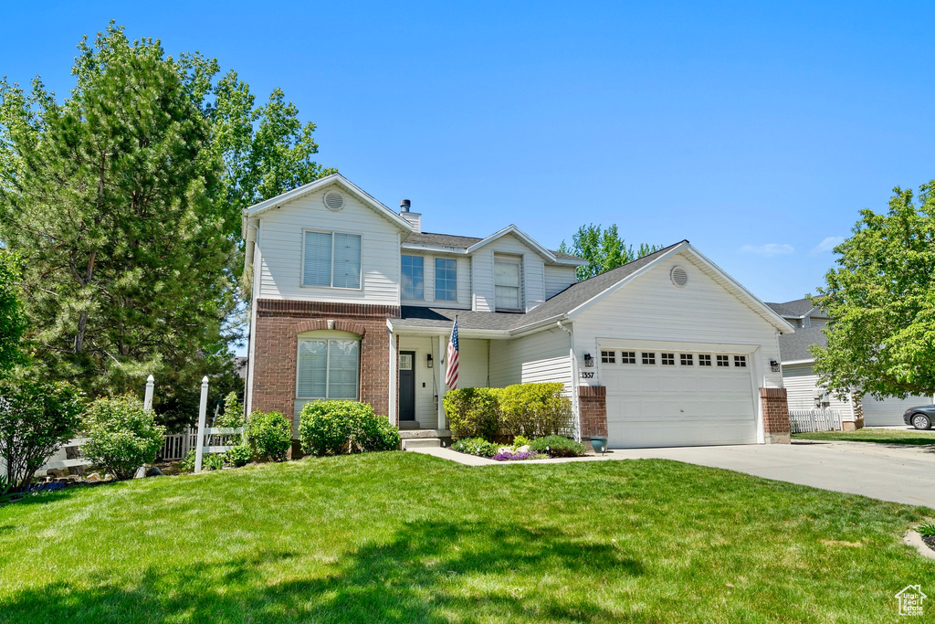 Traditional home featuring concrete driveway, brick siding, an attached garage, and a front yard