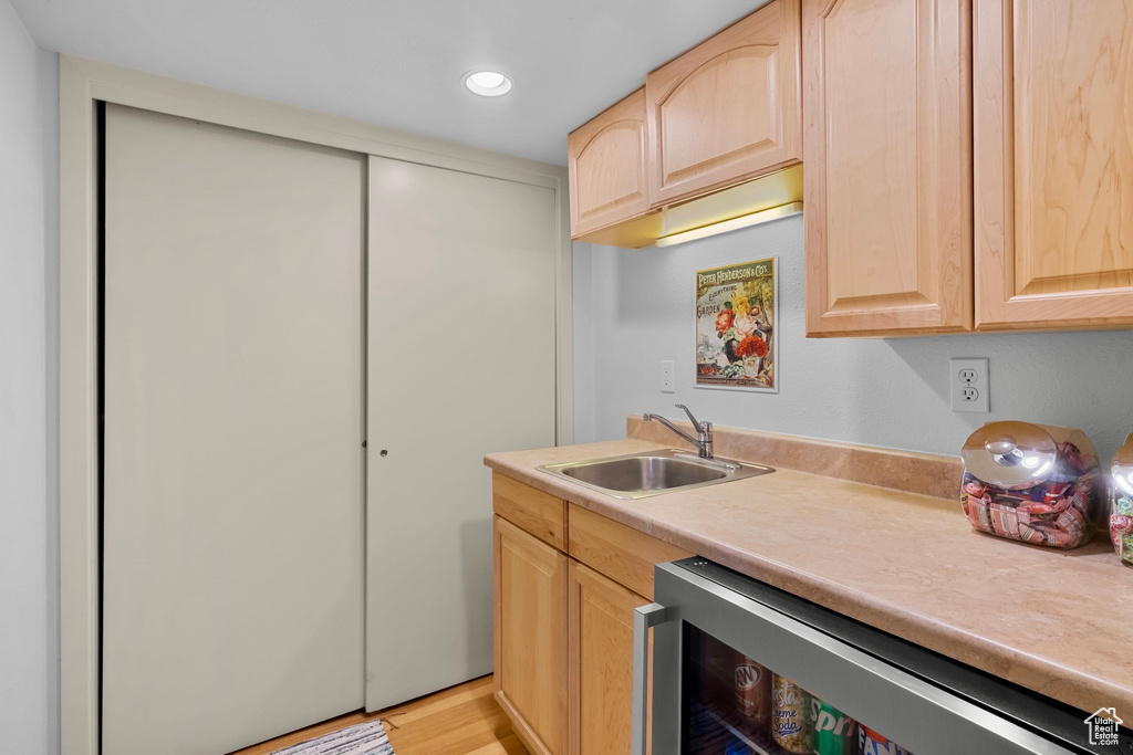 Kitchen featuring a sink, light countertops, beverage cooler, light brown cabinets, and recessed lighting