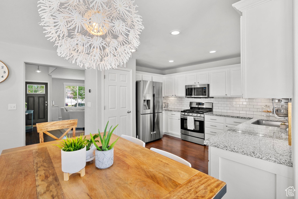 Kitchen with white cabinets, light stone counters, stainless steel appliances, dark wood-type flooring, and backsplash