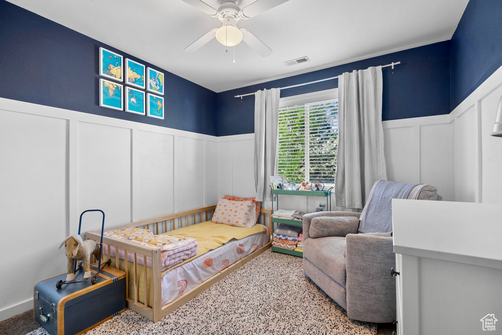 Bedroom featuring ceiling fan, visible vents, wainscoting, and a decorative wall
