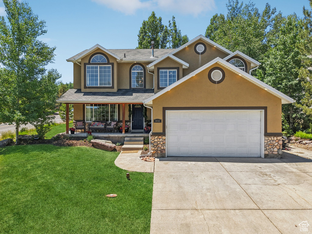 Traditional-style house featuring stucco siding, stone siding, concrete driveway, covered porch, and a front yard