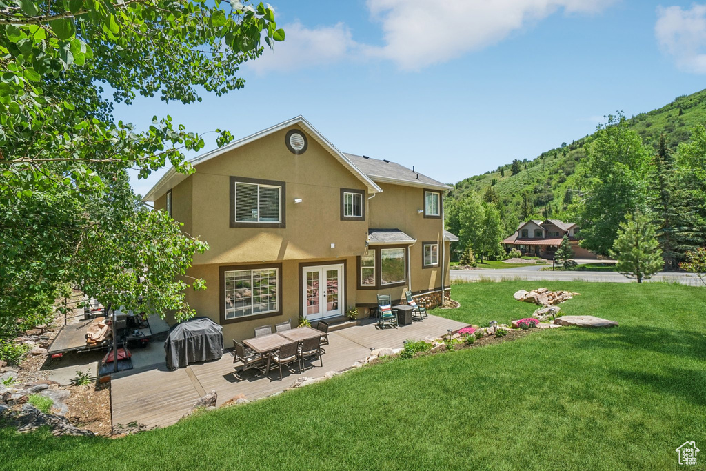 Back of house featuring stucco siding, french doors, a lawn, and a wooden deck