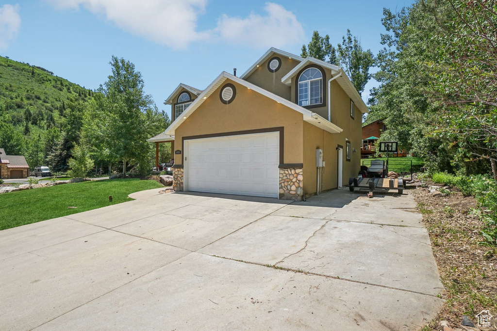Traditional-style house with stucco siding, stone siding, driveway, an attached garage, and a front lawn