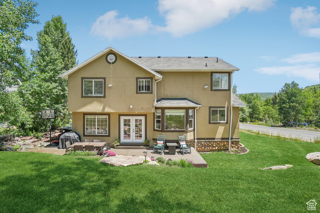 Rear view of property with french doors, stucco siding, a patio area, and a lawn