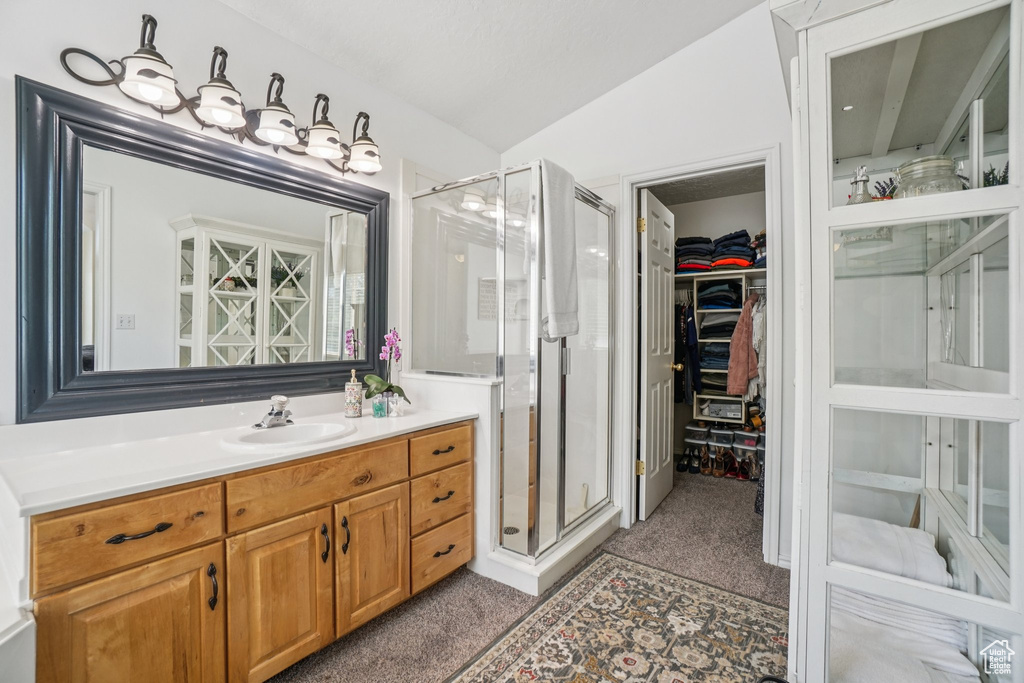 Full bath with a shower stall, vanity, a walk in closet, and lofted ceiling