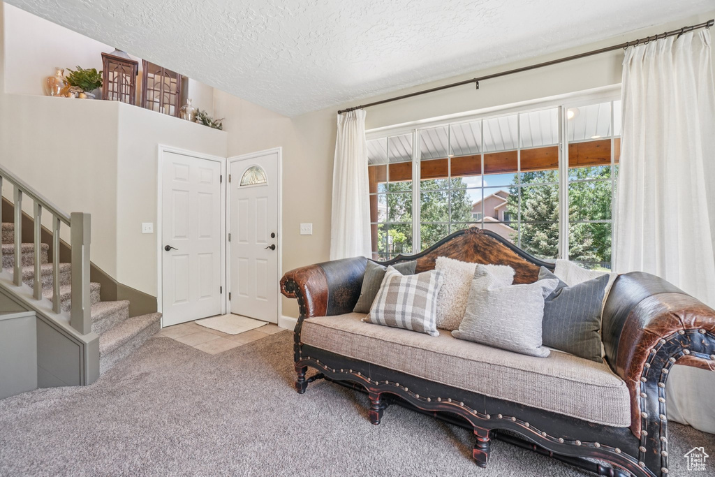 Carpeted living room with a textured ceiling, stairway, and tile patterned flooring