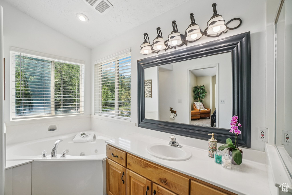 Bathroom featuring vanity, lofted ceiling, and a tub with jets