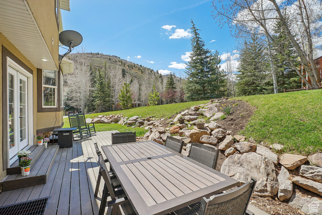 Wooden deck with a mountain view, outdoor dining area, and a yard