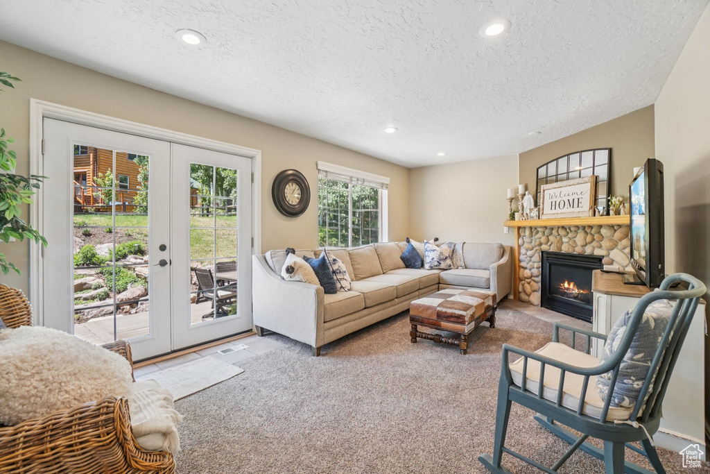 Carpeted living area with a textured ceiling, french doors, a stone fireplace, and recessed lighting