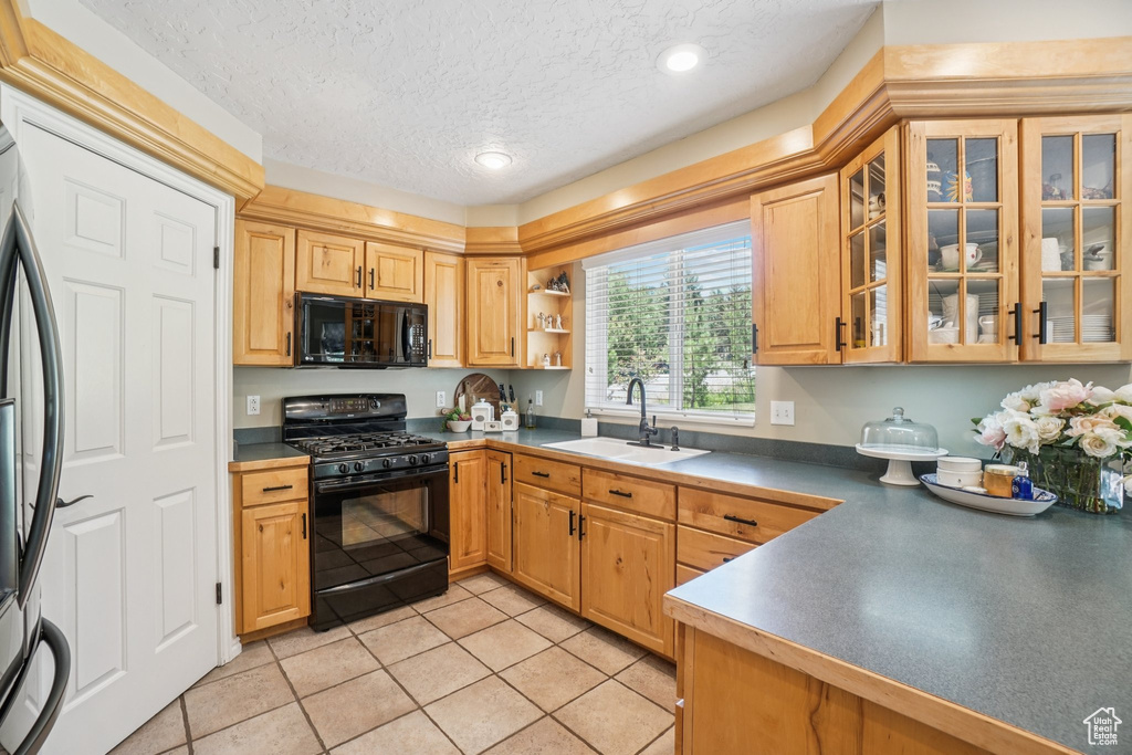 Kitchen with black appliances, light tile patterned floors, a textured ceiling, glass insert cabinets, and dark countertops