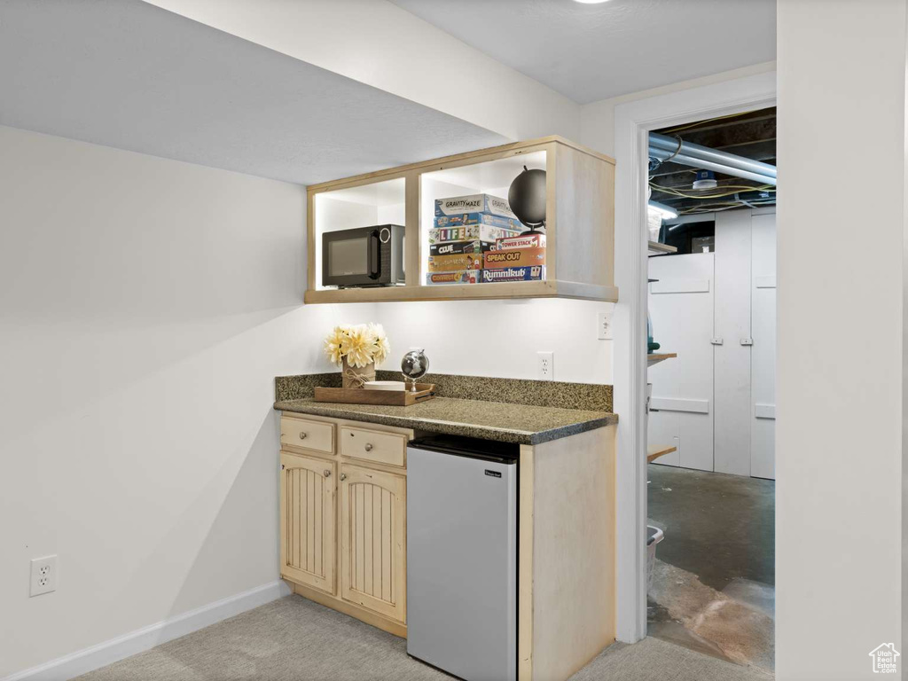 Bar featuring freestanding refrigerator, concrete flooring, wet bar, and black microwave