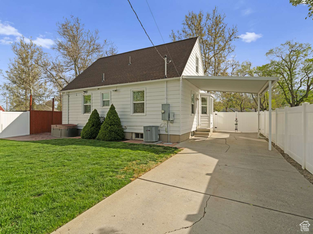 Rear view of property featuring a carport, a hot tub, central air condition unit, a fenced backyard, and concrete driveway