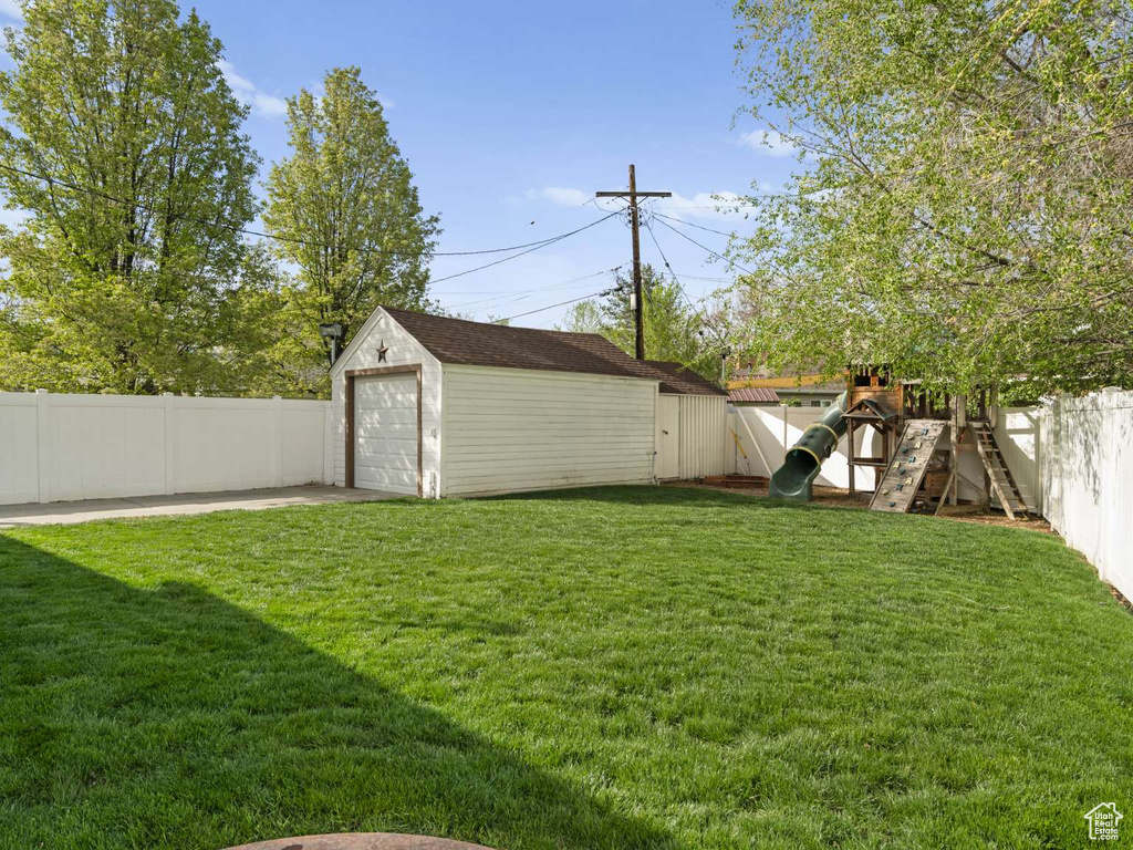 View of yard featuring a detached garage, an outbuilding, a fenced backyard, and a playground
