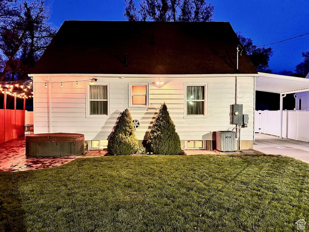 Back of property with a lawn, a hot tub, and fence