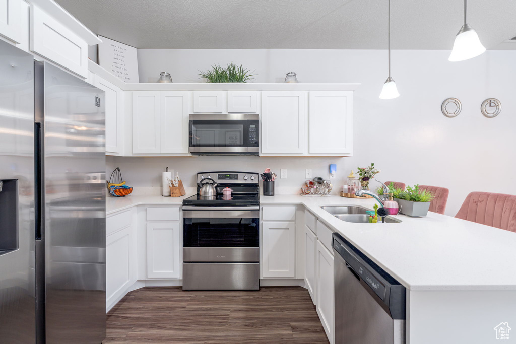 Kitchen featuring appliances with stainless steel finishes, a sink, light countertops, a peninsula, and white cabinetry