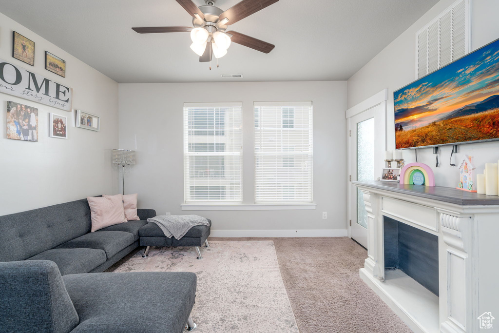 Living area featuring ceiling fan, visible vents, a fireplace, baseboards, and light carpet