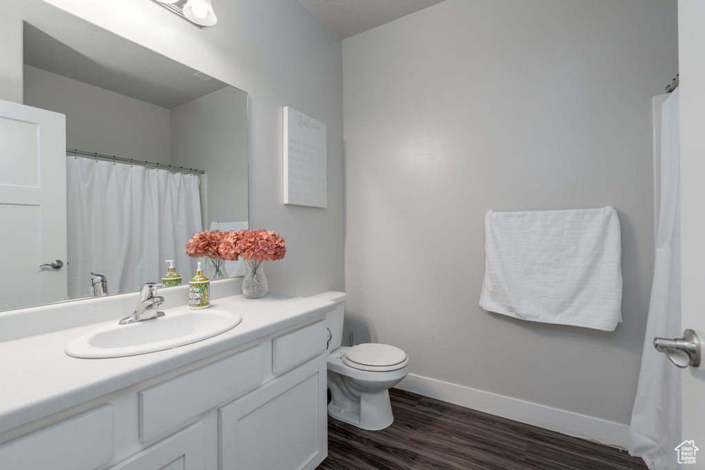 Full bathroom with baseboards, wood finished floors, toilet, and vanity