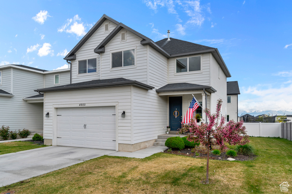 Traditional-style house featuring roof with shingles, a front yard, fence, concrete driveway, and an attached garage