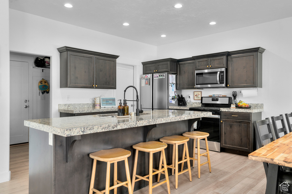 Kitchen featuring recessed lighting, appliances with stainless steel finishes, a breakfast bar area, and light wood-type flooring