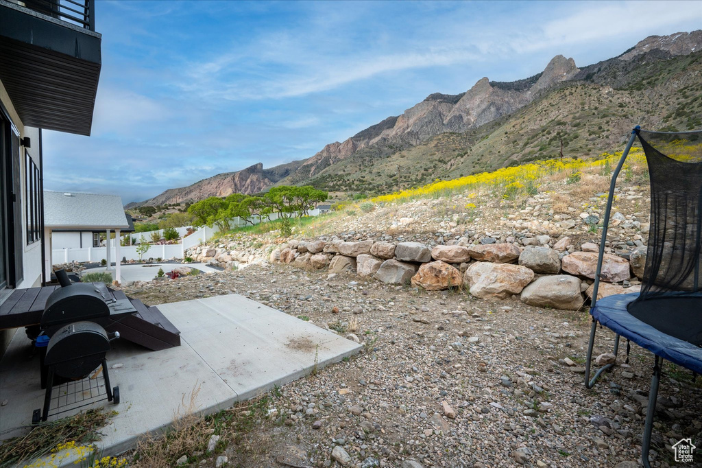 View of yard featuring fence, a mountain view, a trampoline, and a patio area