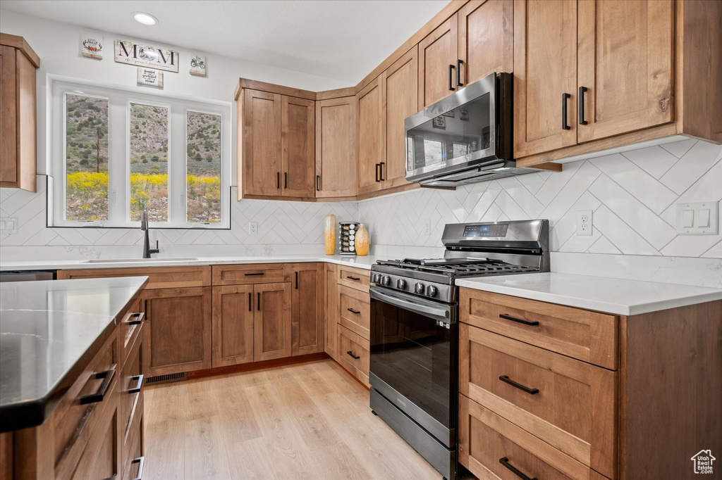 Kitchen with a sink, light wood finished floors, light countertops, stainless steel appliances, and tasteful backsplash