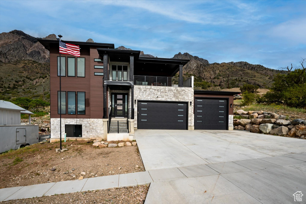 Contemporary home with an attached garage, stone siding, a mountain view, a balcony, and driveway