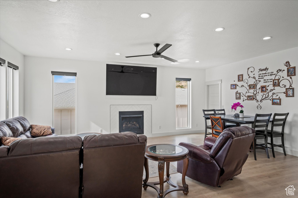 Living room with ceiling fan, a fireplace, baseboards, light wood-style floors, and recessed lighting