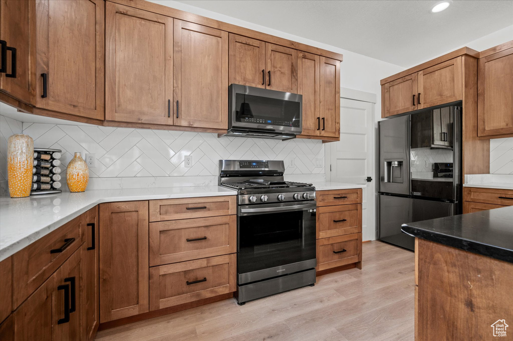 Kitchen with brown cabinetry, recessed lighting, light wood-type flooring, tasteful backsplash, and appliances with stainless steel finishes
