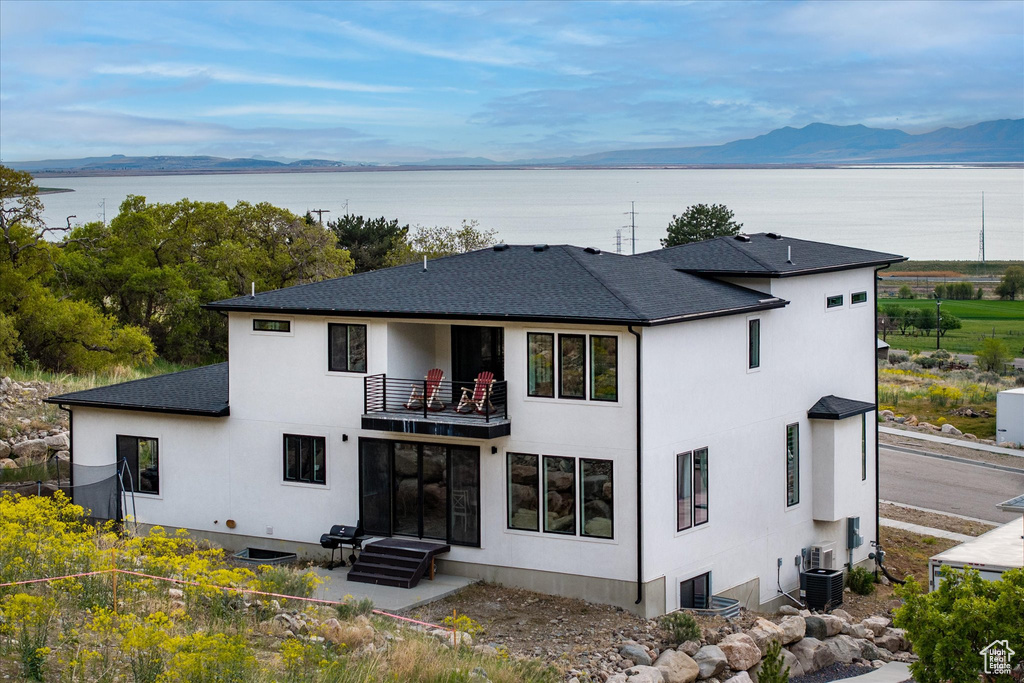 Back of property featuring a shingled roof, a balcony, central AC unit, and stucco siding