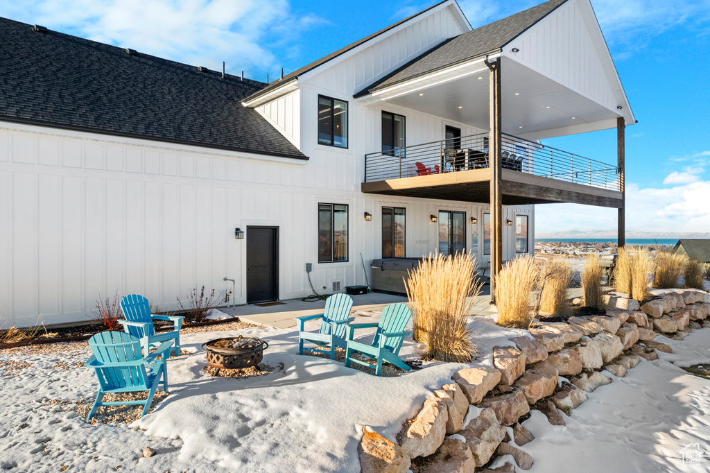 Rear view of property with board and batten siding, a patio area, a balcony, an outdoor fire pit, and a shingled roof