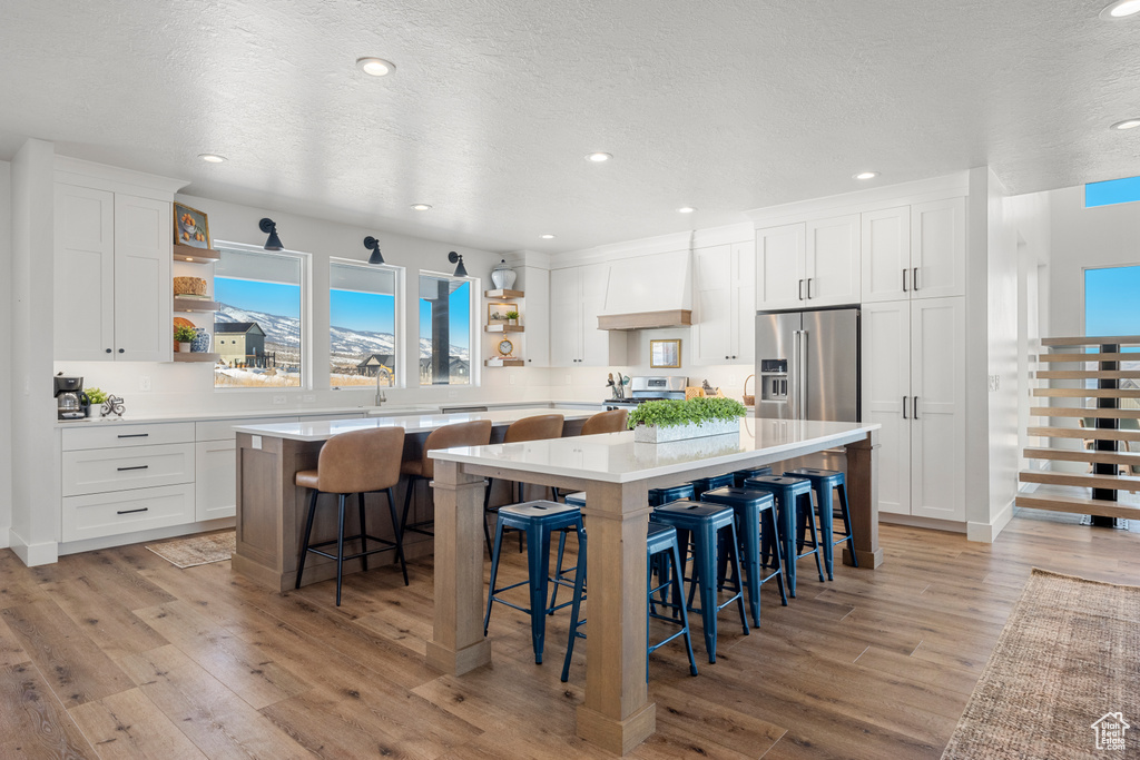 Kitchen with white cabinetry, open shelves, appliances with stainless steel finishes, and a large island