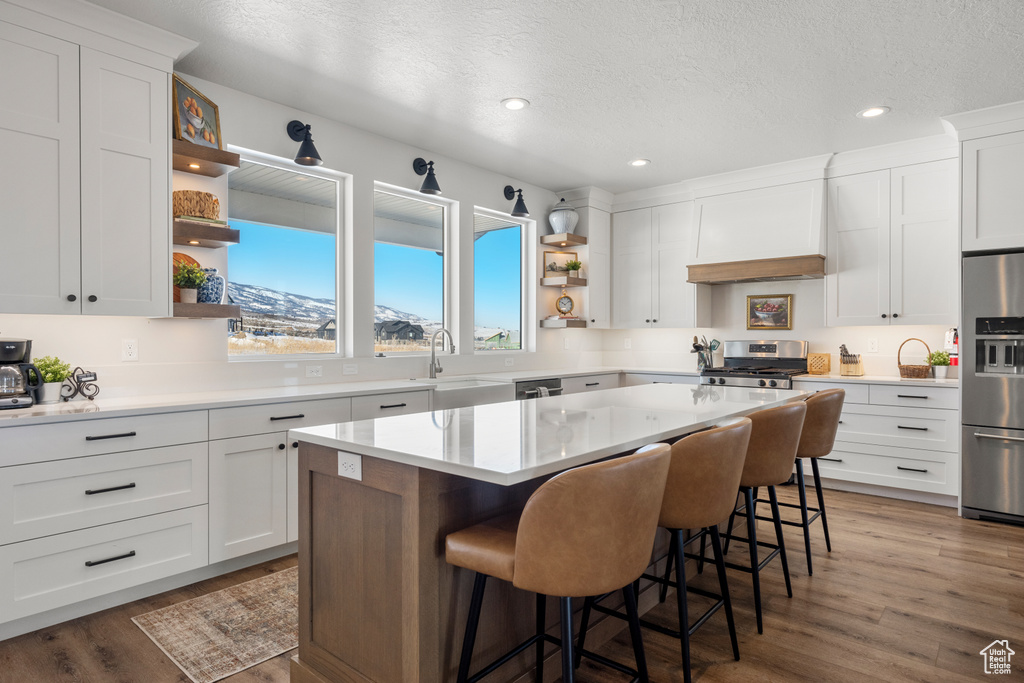 Kitchen featuring a kitchen breakfast bar, a textured ceiling, open shelves, white cabinets, and stainless steel appliances