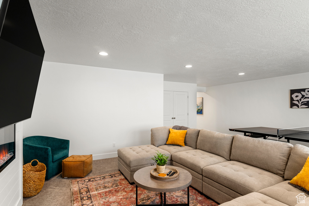 Living room with a glass covered fireplace, baseboards, recessed lighting, a textured ceiling, and carpet flooring