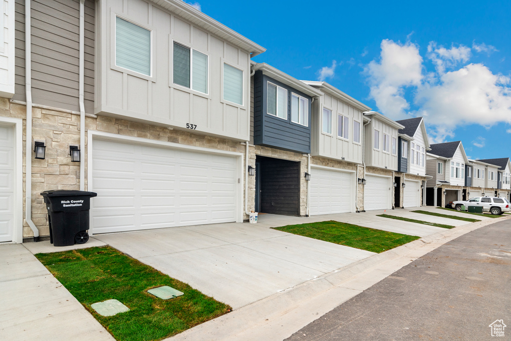 View of property with a residential view, an attached garage, stone siding, board and batten siding, and driveway