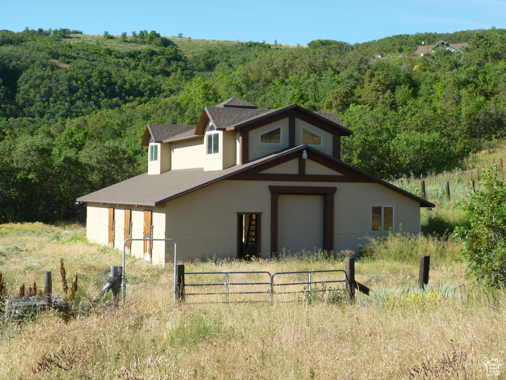 Exterior space with roof with shingles, a forest view, stucco siding, and fence
