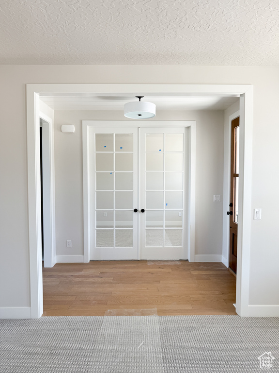 Entrance foyer featuring light wood-style floors, baseboards, french doors, and a textured ceiling