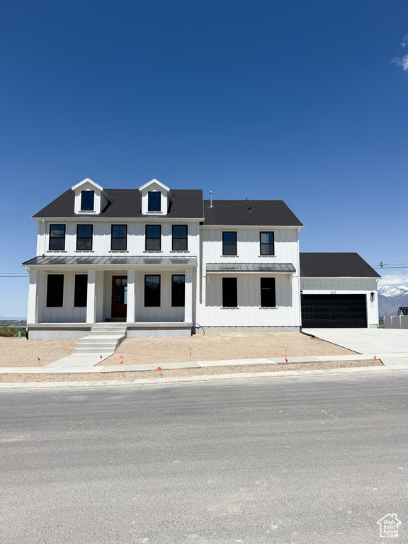 View of front facade featuring an attached garage, board and batten siding, a standing seam roof, covered porch, and metal roof