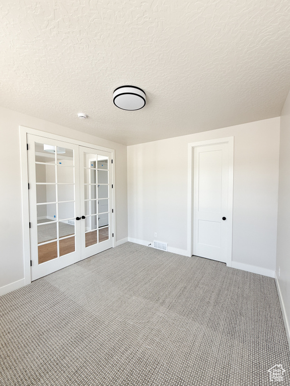 Empty room with french doors, a textured ceiling, visible vents, baseboards, and carpet flooring