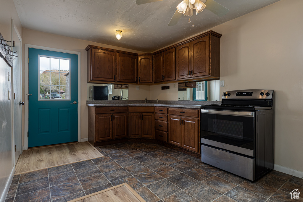 Kitchen featuring stone finish flooring, baseboards, stainless steel electric stove, and ceiling fan