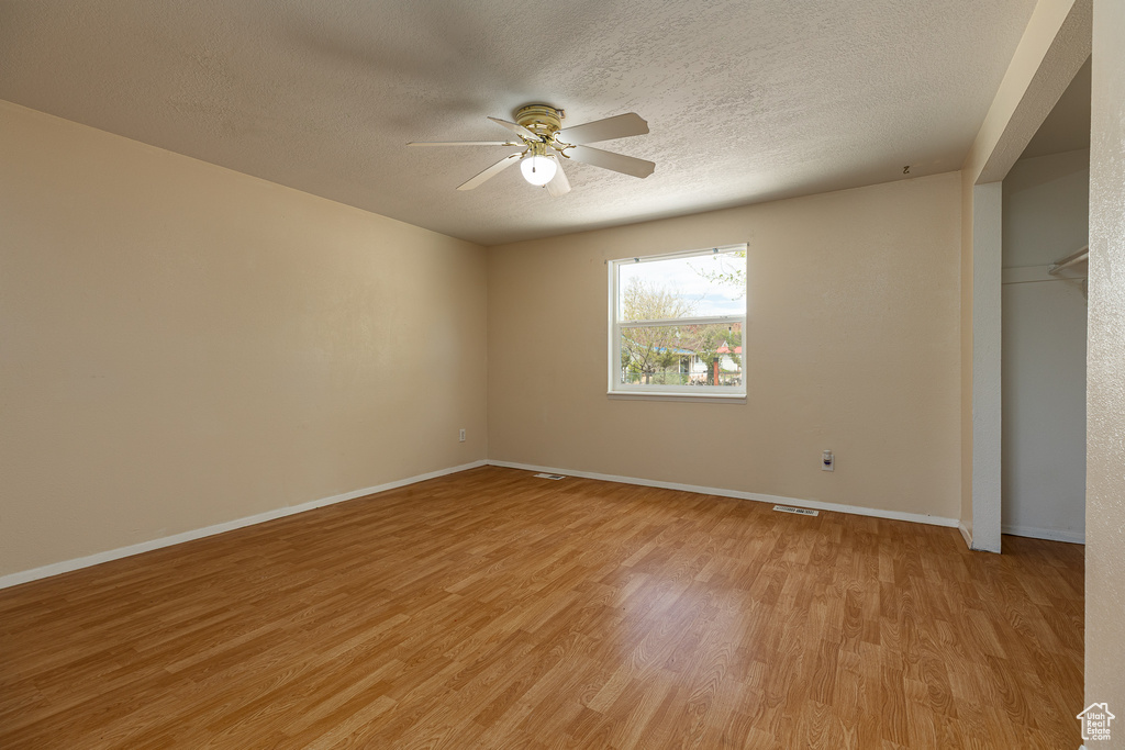 Spare room with ceiling fan, light wood finished floors, a textured ceiling, baseboards, and visible vents