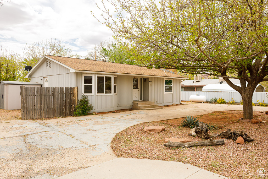Ranch-style home with concrete driveway, fence, and a shingled roof
