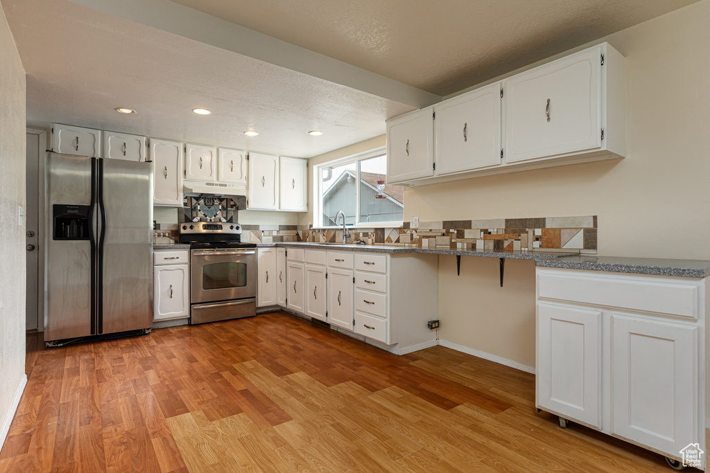 Kitchen with light wood-style floors, stainless steel appliances, white cabinetry, and under cabinet range hood