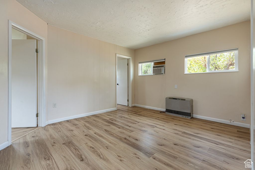 Unfurnished room with light wood-type flooring, a textured ceiling, heating unit, and baseboards